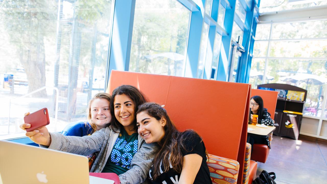 Three students taking a selfie while sitting in a booth in the MU.