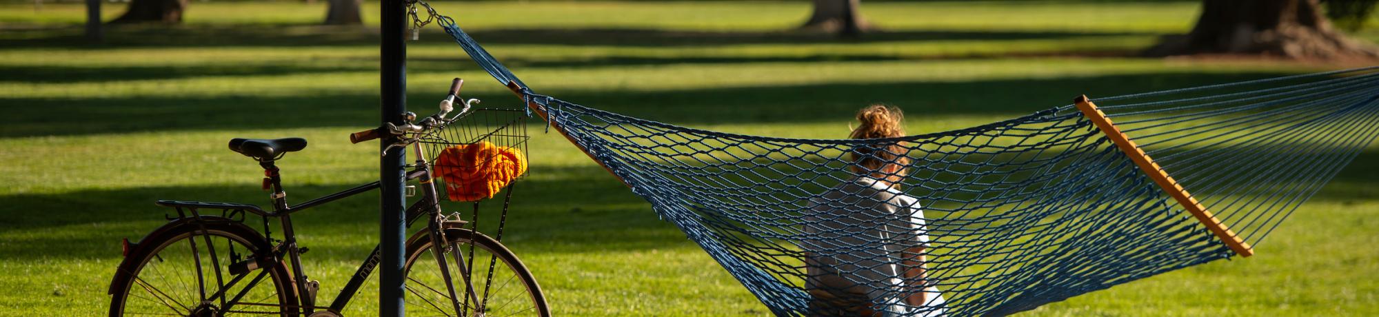 Student sitting in a hammock with a bicycle parked nearby